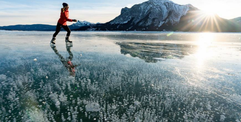 woman ice skating on frozen abraham lake with ice bubbles