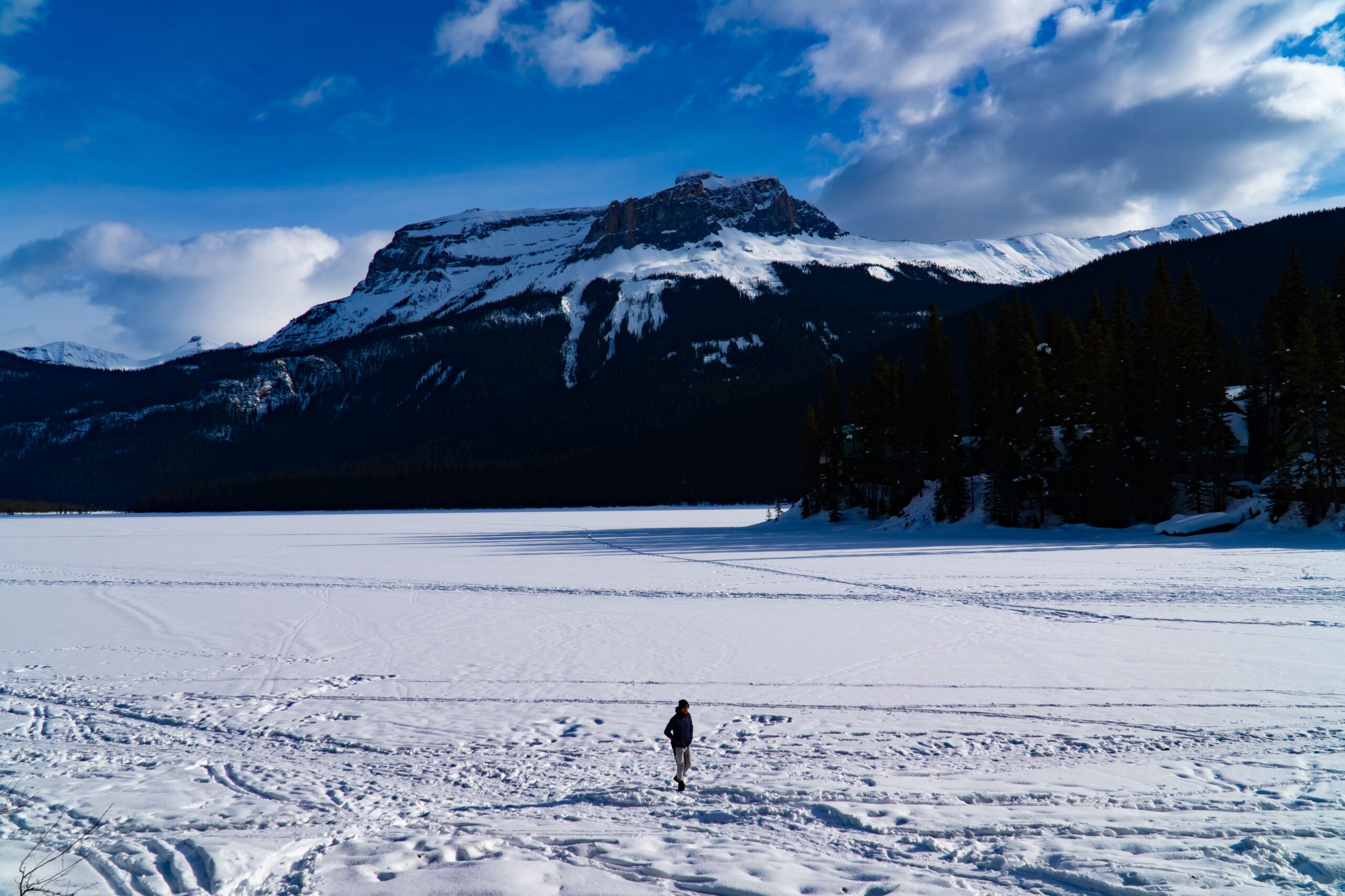 Beautiful view of silhouette of man on frozen snow covered lake on mountains background under blue sky and white clouds