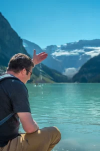 Man sat at the lakeshore of Lake Louise, fingers in the cold water.